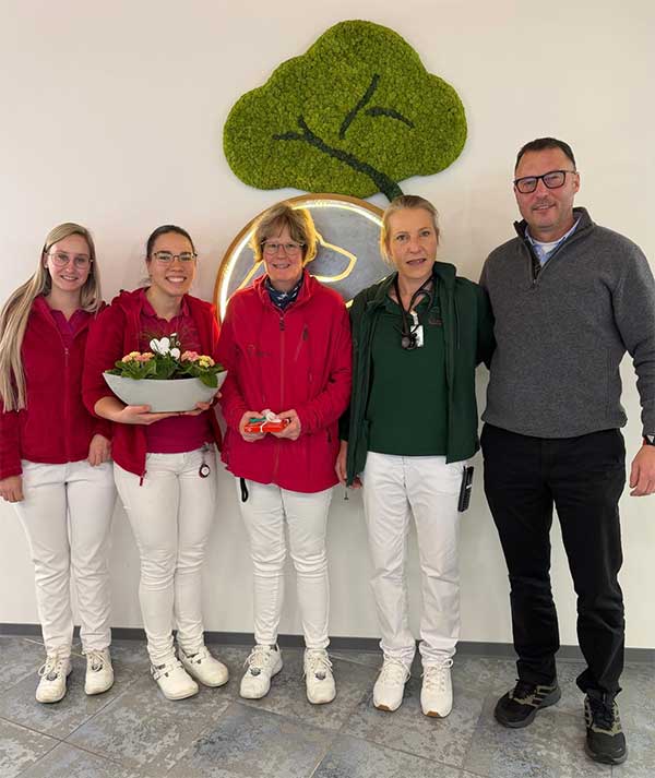 Tierarzt und Tierarzthelferinnen stehen zusammen vor dem Logo der Praxis